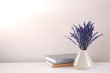 Bouquet of beautiful preserved lavender flowers and notebooks on white table near beige wall, space...