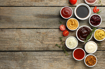 Obraz na płótnie Canvas Different tasty sauces in bowls and ingredients on wooden table, flat lay. Space for text