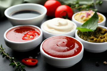 Different tasty sauces in bowls and ingredients on black table, closeup