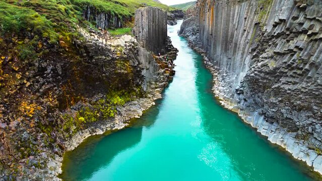 Flying through the Studlagil Canyon with the Jokulsa. Bru river in east Iceland, basalt rocks, Europe. Studlagil basalt rock columns canyon area and a stunning blue-green glacial river.