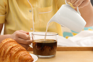 Woman pouring milk into cup with hot drink in bed, closeup