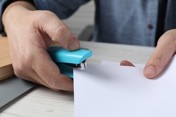 Man with papers using stapler at white table, closeup
