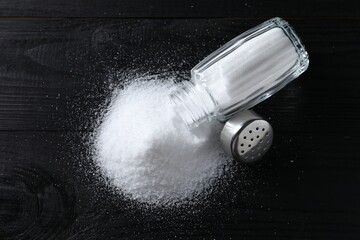 Organic salt in glass shaker on black wooden table, top view