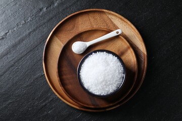 Organic white salt in bowl and spoon on black table, top view