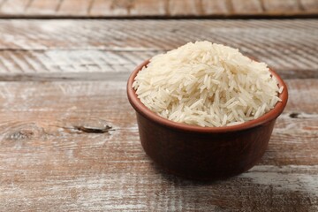 Raw basmati rice in bowl on wooden table, space for text