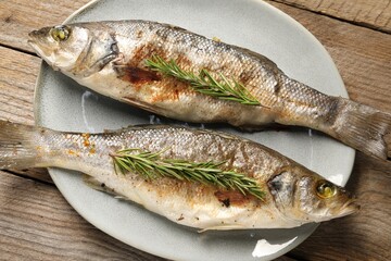 Delicious baked fish and rosemary on wooden table, top view