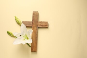 Wooden cross and lily flowers on pale yellow background, top view with space for text. Easter...