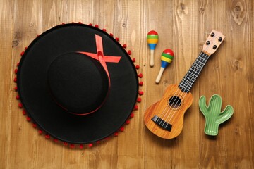 Mexican sombrero hat, maracas, toy cactus and guitar on wooden background, flat lay