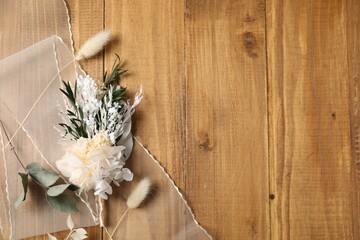 Stylish boutonniere and ribbon on wooden table, top view. Space for text