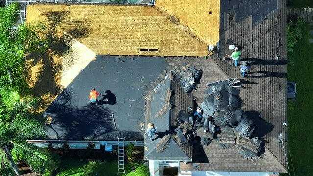 Workers changing old asphalt shingles to new on private house rooftop. Roof repair on Florida home. Real estate development concept