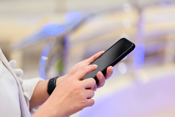 A cropped shot of an Asian woman using her smartphone, reading online articles, or responding to messages while sitting at a cafe in the city.