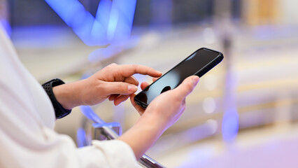 A cropped shot of an Asian woman using her smartphone, reading online articles, or responding to messages while sitting at a cafe in the city.