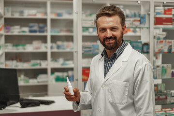 Male pharmacist in white coat holding nose spray while working at a pharmacy