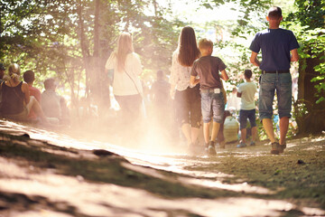 Festival, party and family walking in forest outdoor together for event, celebration or social gathering. Mother, father and children in nature, park or woods for summer entertainment from back - obrazy, fototapety, plakaty