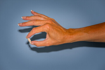 Female hand holding a pill above blue background