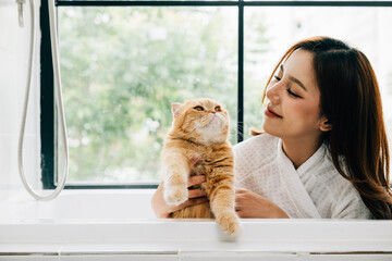 Bath time bonding, a woman holds her Scottish Fold cat in the bathtub, radiating happiness and the...