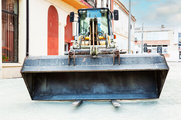 A yellow wheeled bulldozer with a front bucket stands in the city on a construction site.