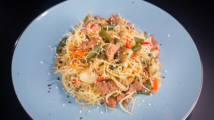 funchoza with meat and vegetables on a blue plate dark background