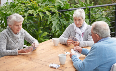 Elderly people, card games and coffee at table with outdoor background for retirement and old age. Group, seniors or family with beverages and thinking for poker, relax and break together on patio