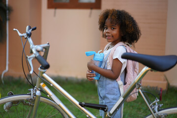 Obraz premium Back-to-school season with african american kid girl on the move with book and colorful school backpack, children, education, student go to school, study and learn at primary school