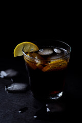 Glass of cola with lemon and ice cubes. Dark stone background. Close up.	