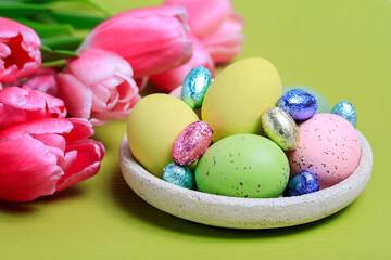 Bouquet of pink tulips and bowl with hen and chocolate eggs. Traditional Easter decoration.