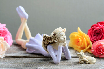 A charming figurine of an angel with a kitten on a wooden table, roses around.
