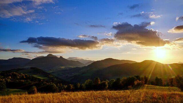 Timelapse with a hilly rural landscape, with colorful clouds in motion at sunset.