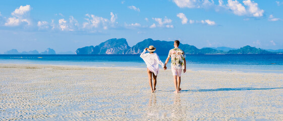 rear view of a couple of men and women walking at the beach at sunset, Koh Kradan island in...