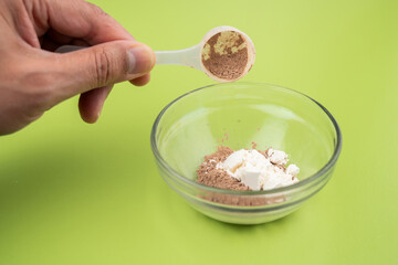 Close-up of serving a portion of protein powder and creatine Into the shaker glass, protein shake on a green table