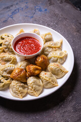 Uzbek samsas and manti with meat, pumpkin and greens on a plate with red sauce