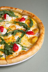 Freshly baked pizza with strawberries, cream cheese and arugula on a white plate. view from above
