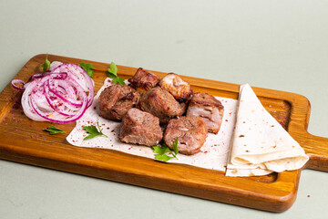 Lamb skewers with grilled vegetables and pita bread on a wooden board.