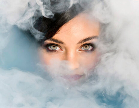 Detail taken from above of a woman's face emerging from a sea of white smoke. Parts of her face partially covered and high iris detail. Magnetic eyes and eyelashes of a model.