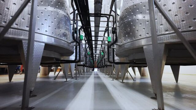 Metal barrels for fermentation, distillation and storage of high quality wine, metal tanks with black pipes and different technical regulators on winemaking factory, viticulture and winery concept