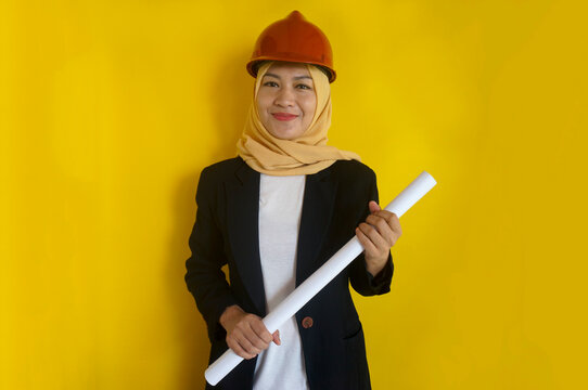 Portrait of smiling constructor worker muslim woman with clipchart and safety helmet standing isolated on yellow background.