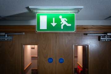 Shallow focus of a generic green, illuminated Fire Escape sign seen next to fire doors in a luxury...