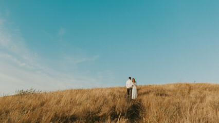 Couple standing on the top of the hill in the wheat meadow. Beautiful landscape of deep blue sky and wheat field. Couple hugs in the middle of nature. couple outdoors enjoying the fresh air

