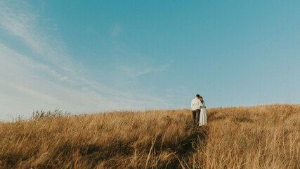 Couple standing on the top of the hill in the wheat meadow. Beautiful landscape of deep blue sky...