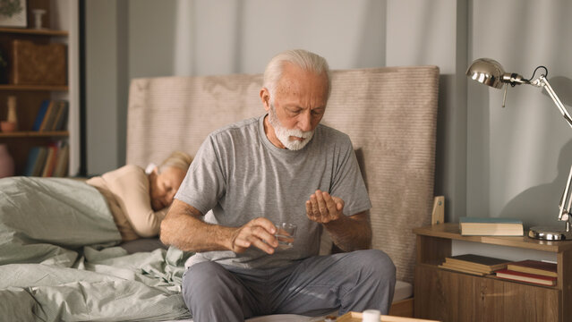 Elderly man taking medication with water in bedroom