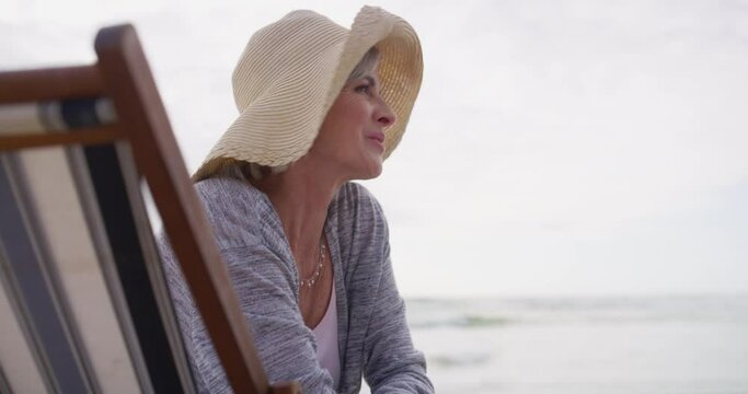 Happy, old woman and relax at beach on holiday in chair and thinking of retirement with freedom or laugh. Summer, vacation and senior smile at ocean or travel at sea on funny adventure or trip