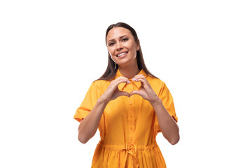 young woman dressed in a summer yellow dress shows a heart with her hands on a white background