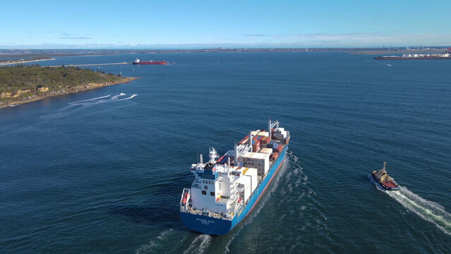 Aerial view of a large cargo container ship entering Botany Bay at the coastline of Kurnell and headland of Kamay Botany Bay National Park, Sydney, NSW heading to Port Botany on a sunny day  