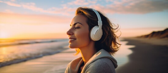 Woman wearing headphones, enjoying wellness, mental health, and fitness on beach during morning,...