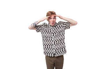 young shocked caucasian man with red hair and a tattoo on his arms in a shirt and trousers