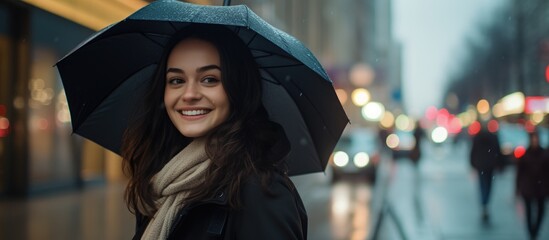 Obraz premium Smiling young woman in warm clothes holding umbrella on city street.