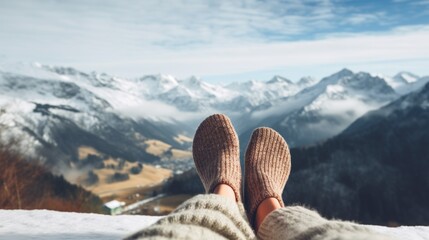 Women's feet in cozy warm wool socks against the backdrop of the high snowy mountains of the Alps and the blue sky. The concept of winter holidays, Travel, Vacations in Nature. - obrazy, fototapety, plakaty