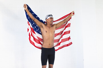 Young biracial male athlete swimmer celebrates with an American flag, with copy space
