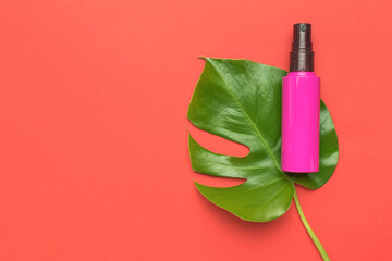 A red bottle with lotion spray on a green leaf on a red background.