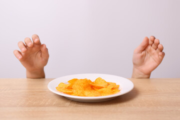Children's hands are visible from under the table, trying to take potato chips from the table.